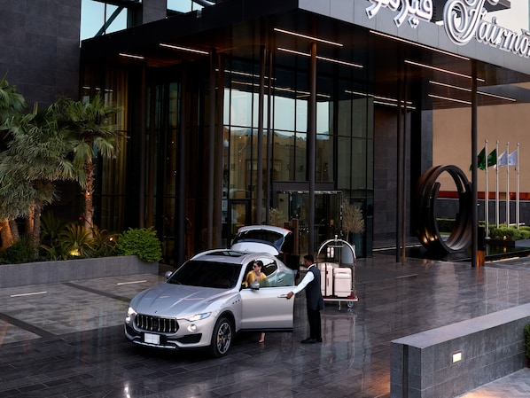 A modern hotel entrance with a sleek car parked in front, a luggage cart, and a well-maintained garden area. - Fairmont Ramla Riyadh (Riyadh)