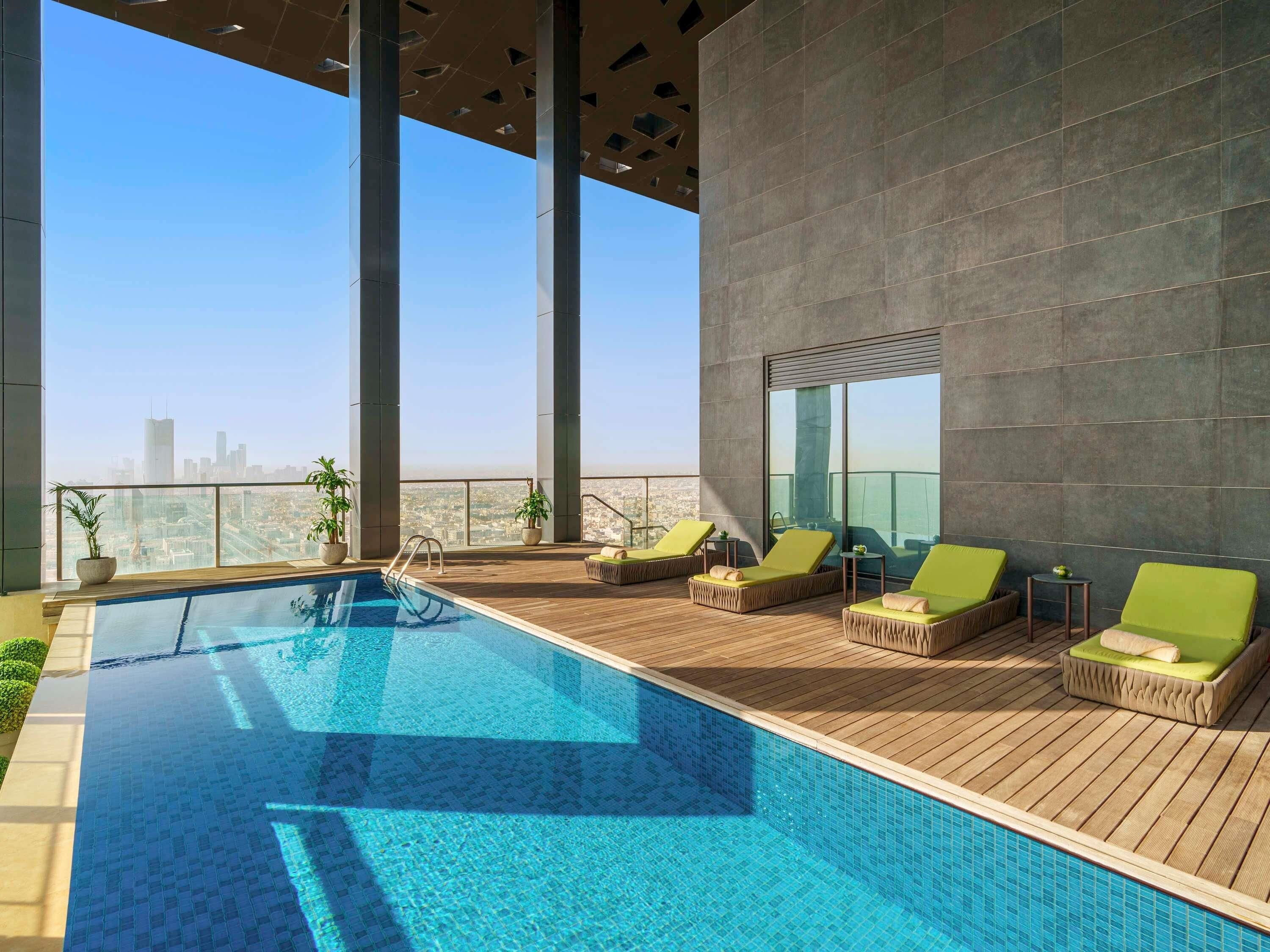 Piscina no terraço com água azul cristalina, rodeada por um deck de madeira e espreguiçadeiras verdes.