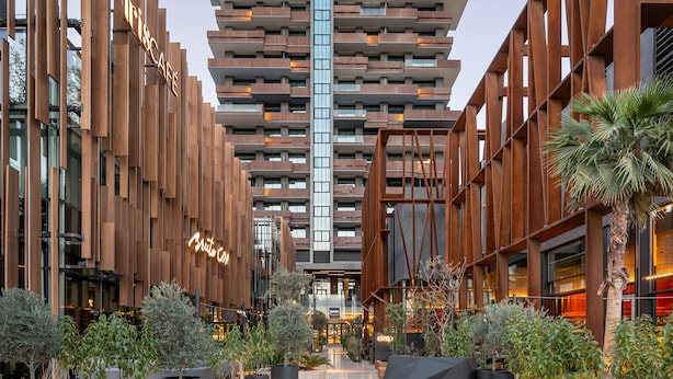 A modern building with a central glass elevator shaft, surrounded by wooden paneling and potted plants. - Fairmont Ramla Riyadh (Riyadh)