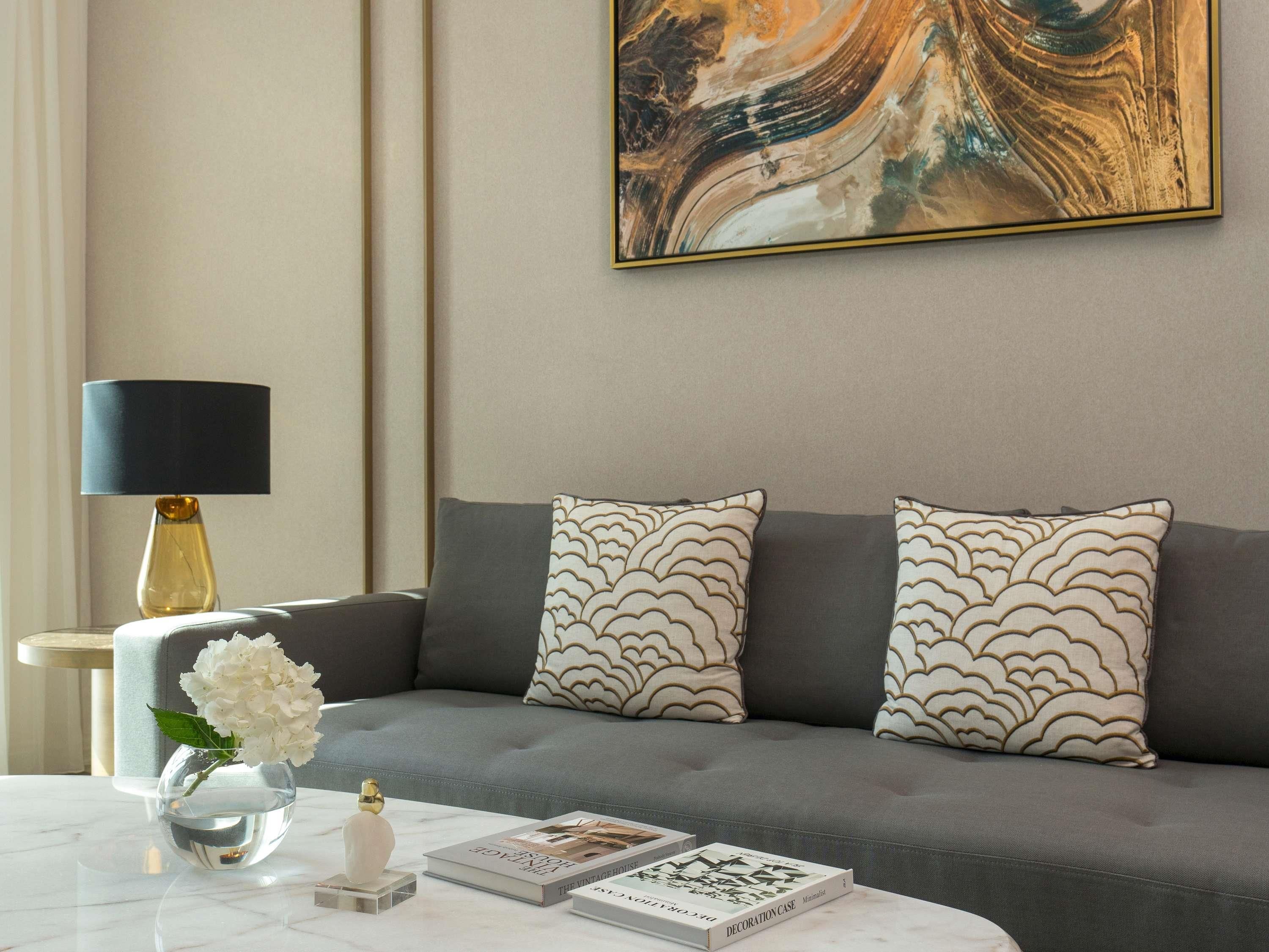 A modern living room with a grey sofa, patterned cushions, a clear vase with flowers, and a marble coffee table.
