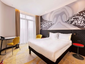 Relax in comfort with a large bed, a small table, and a desk, surrounded by a unique mural and a view of the outdoors.