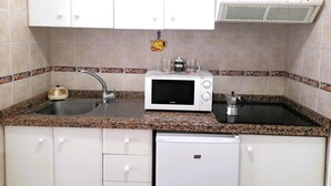 Eine kompakte Küche mit weißen Schränken, einer Granit Arbeitsplatte, einer Mikrowelle, einem Toaster, einem Spülbecken und einem Geschirrspüler.