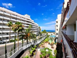 Un hotel de varios pisos con balcones, piscina y palmeras.