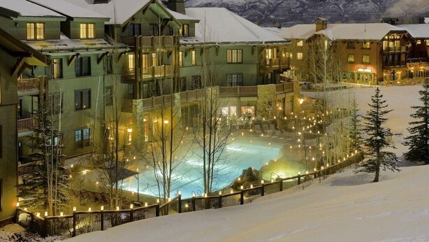 A snow-covered outdoor pool surrounded by multi-story buildings with balconies, set against a mountainous backdrop. - Ritz Carlton Luxury 3 Bedroom (Aspen)