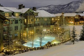 A snow-covered outdoor pool surrounded by multi-story buildings with balconies, set against a mountainous backdrop. - Ritz Carlton Luxury 3 Bedroom (Aspen)