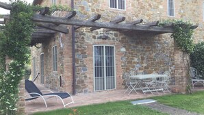 Ein Steinhaus mit einer Pergola, Außenbestuhlung und einer Rasenfläche.