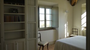 Ein Schlafzimmer mit Bett, Fenster, Stuhl und Bücherregal.