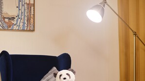 A room with a blue armchair, a panda plush toy, a lamp, and a cow-patterned blanket. - TORA Hotel Ueno 193 A (Tokyo)