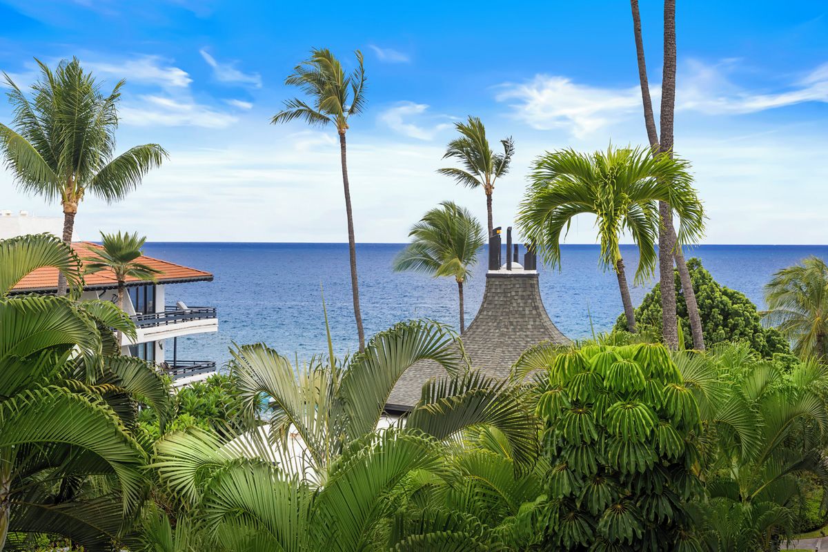 A coastal property with a view of the ocean, palm trees, and a building with a red roof.