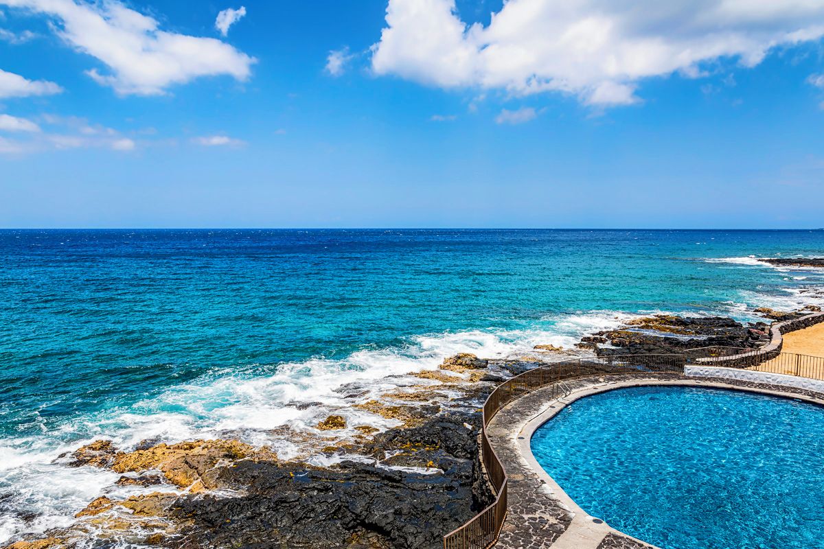 Ein Poolbereich an der Küste mit freiem Blick auf das Meer und eine felsige Küstenlinie.