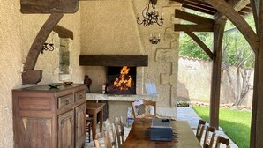 Un patio al aire libre con suelo de piedra, mobiliario de madera, una chimenea y un muro de piedra.