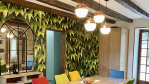 Un comedor con una gran mesa de madera, sillas coloridas y una pared cubierta de hojas verdes.