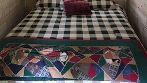 Una habitación acogedora estilo cabaña, con colcha a cuadros, un cubrecama de patchwork y un cuadro enmarcado sobre la cama.