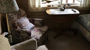 Una habitación de cabaña acogedora con interior de madera, un escritorio con lámpara, una silla y una cama.
