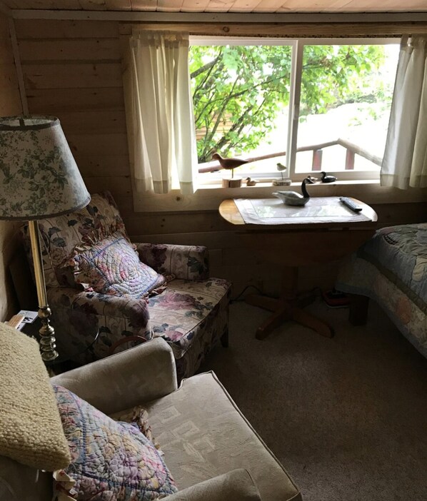 Una habitación de cabaña acogedora con interior de madera, un escritorio con lámpara, una silla y una cama.