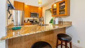 A kitchen with wooden cabinets, stainless steel appliances, a granite countertop, and a bar stool.
