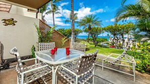 A covered outdoor seating area with a table and chairs, overlooking a lush garden and the ocean.