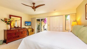 A hotel room with a large bed, a ceiling fan, a TV, a dresser, and a sliding door to a balcony.