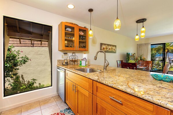 A kitchen with granite countertops, wooden cabinets, a built-in dishwasher, and pendant lighting.