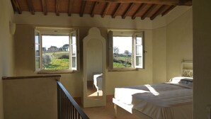 Un dormitorio con una cama, dos ventanas que dan a un paisaje verde y un techo de madera.