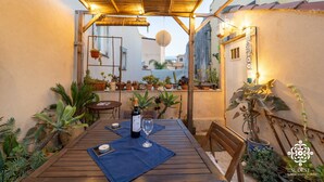 A wooden table with a bottle of wine and a glass, surrounded by potted plants and a pergola with lights. - Casa Sophia (Syracuse)