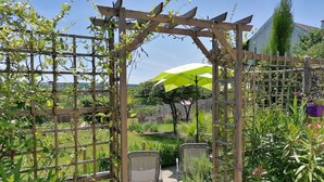 A wooden pergola with climbing plants, a pathway leading to a seating area, and a green umbrella providing shade. - Gîte 3 Personnes, Proche de Beauval et Chenonceaux (Montrichard Val de Cher)