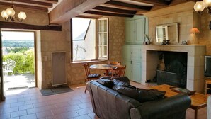 A rustic interior with exposed wooden beams, a fireplace, a dining area, and a view through a large window. - Gîte 3 Personnes, Proche de Beauval et Chenonceaux (Montrichard Val de Cher)