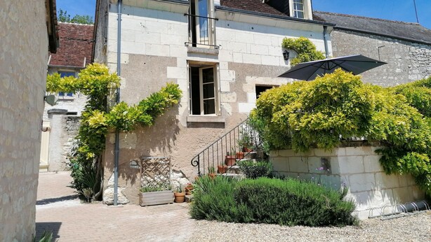 A two-story house with a stone facade, a wooden door, and a small balcony. There is a garden with various plants and a gravel pathway leading to the entrance. - Gîte 3 Personnes, Proche de Beauval et Chenonceaux (Montrichard Val de Cher)