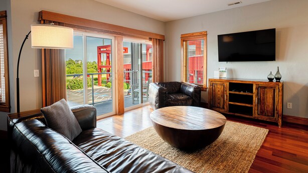A modern living room with a leather sofa, a round coffee table, and a TV mounted on the wall. - 3-Bedroom, 2.5-Bathroom Suite at REAL Watersports (Waves)