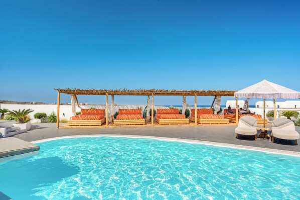 Un área junto a la piscina con sillones de descanso y una pérgola.
