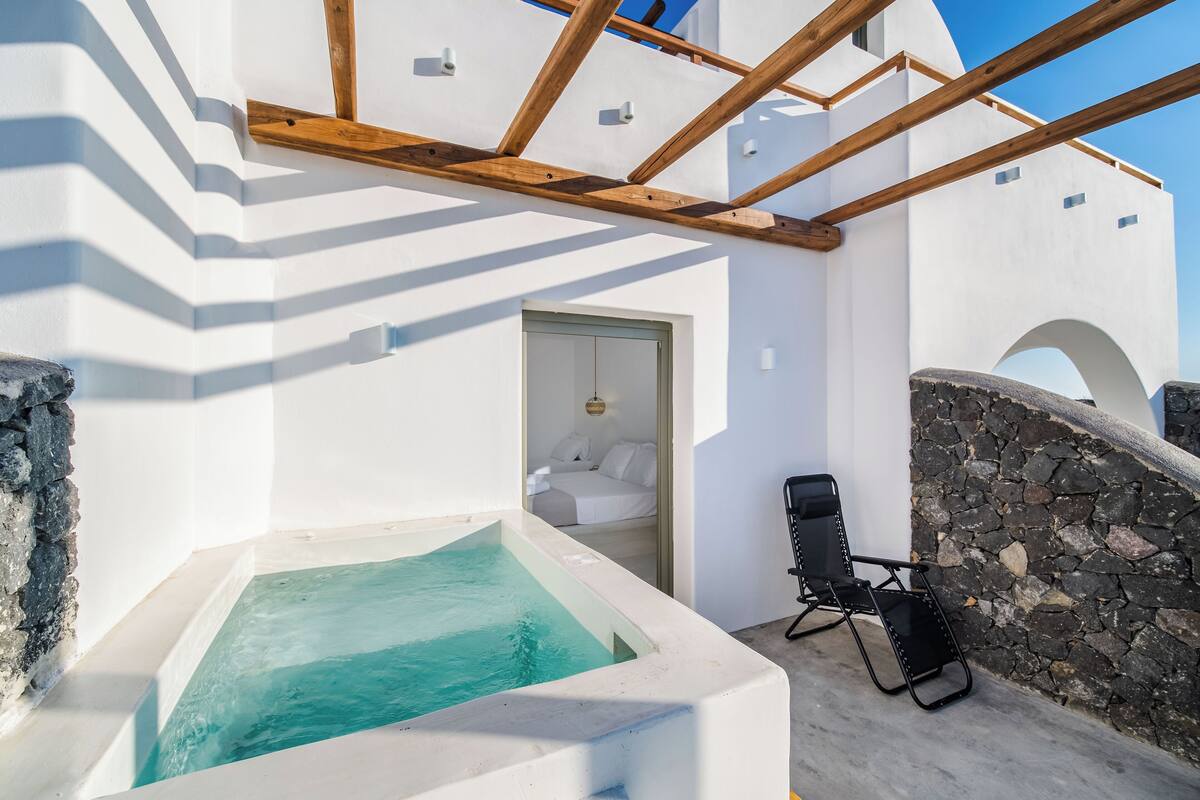A white building with a stone wall, a wooden ceiling, and a small pool.