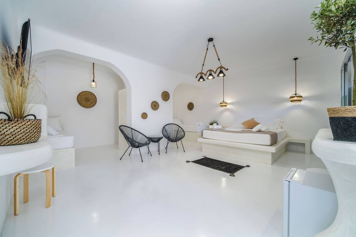 A modern living room with a white sofa, two black chairs, a coffee table, and a hanging light fixture.