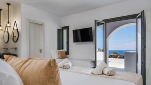 Habitación de hotel con cama, televisor, puerta y vista al mar.