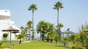 A resort with palm trees, thatched umbrellas, and a white building. - Casares Del Mar (Casares)