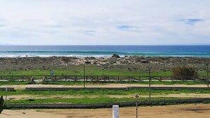 Blick auf einen Strand mit Sandfläche, einem Zaun und einem Parkschild.