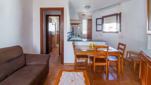 Ein Wohnzimmer mit braunem Sofa, einem Esstisch mit Stühlen und einer Küchenzeile mit Fenster.