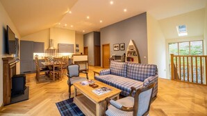 A spacious living area with a sofa, chairs, a coffee table, and a dining table. There is a kitchen in the background with cabinets and a window.