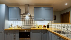 A modern kitchen with grey cabinets, a stainless steel range hood, a wooden countertop, and a built-in dishwasher.