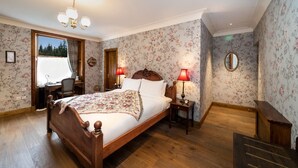 Een slaapkamer met een houten bed, twee nachtkastjes met lampen, bloemenbehang, een raam met uitzicht en een spiegel aan de muur.