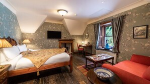 A cozy bedroom with a wooden bed, a red sofa, a small table, and a window with curtains. - Rhododendron Suite -With views of the rhododendron trees on the hillside (Inverness)