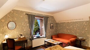 A cozy room with a wooden desk, a chair, a red sofa, a small table, and a window with curtains. - Rhododendron Suite -With views of the rhododendron trees on the hillside (Inverness)