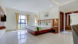 Habitación de hotel con una cama grande, una mesita de noche, un televisor montado en la pared y una ventana con cortinas.