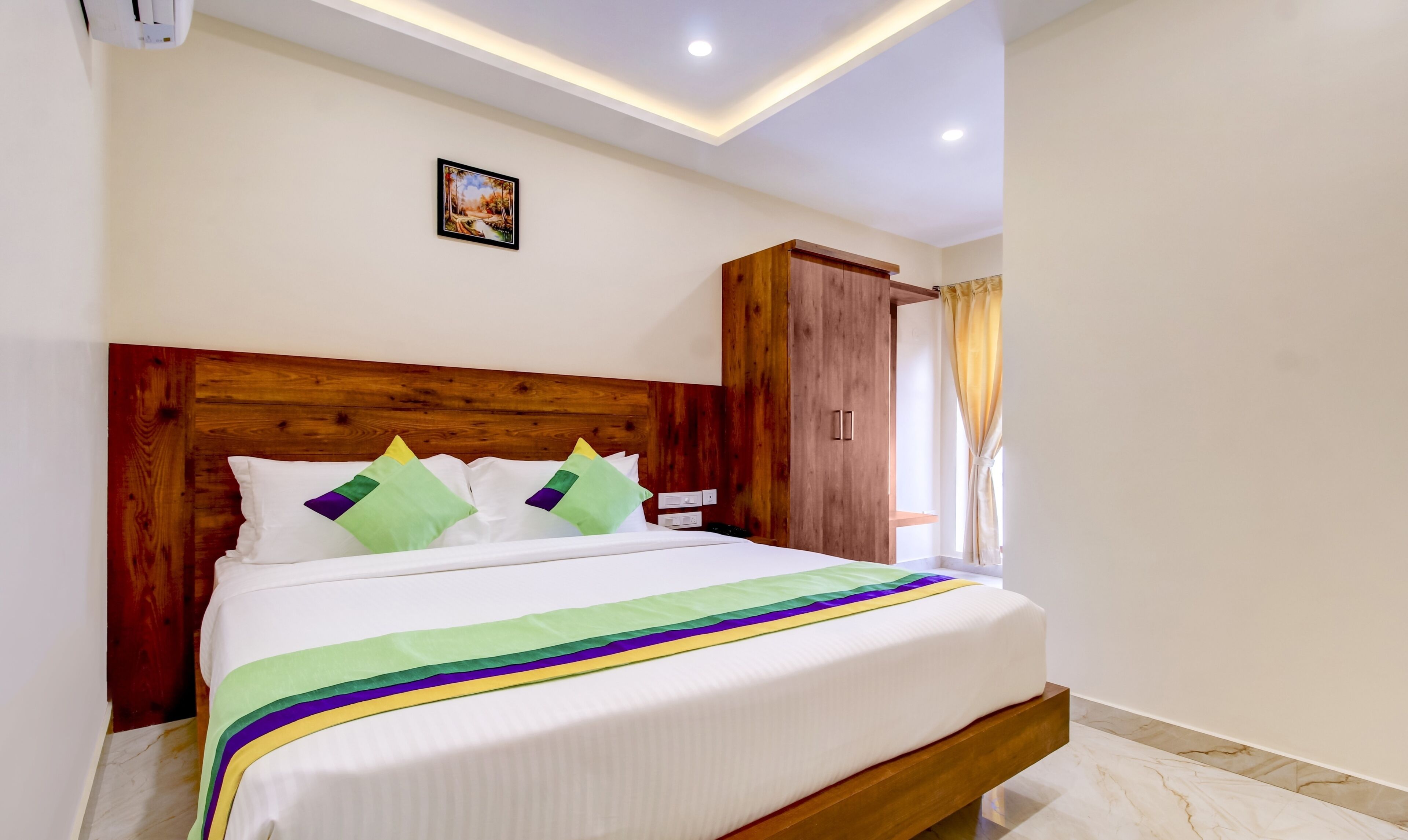 Una cama bien hecha con cabecera de madera, un cuadro en la pared y una ventana con cortinas.