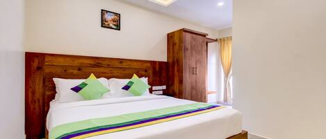 Una cama bien hecha con cabecera de madera, un cuadro en la pared y una ventana con cortinas.