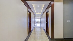 Un pasillo largo y estrecho con puertas de madera a ambos lados, piso de baldosas brillantes e iluminación empotrada en el techo.