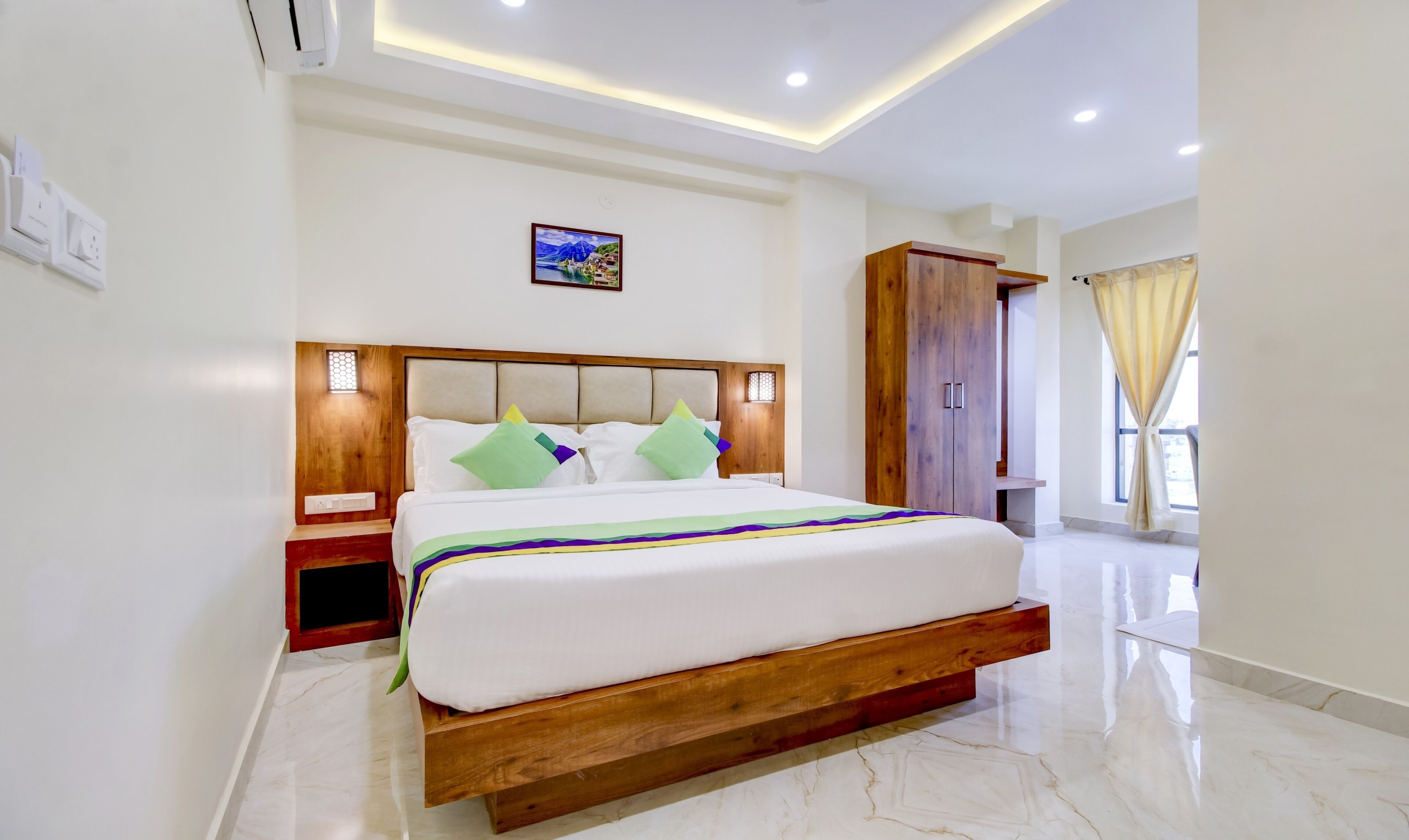 A modern hotel room with a large bed, wooden headboard, and a view of the city through the window.