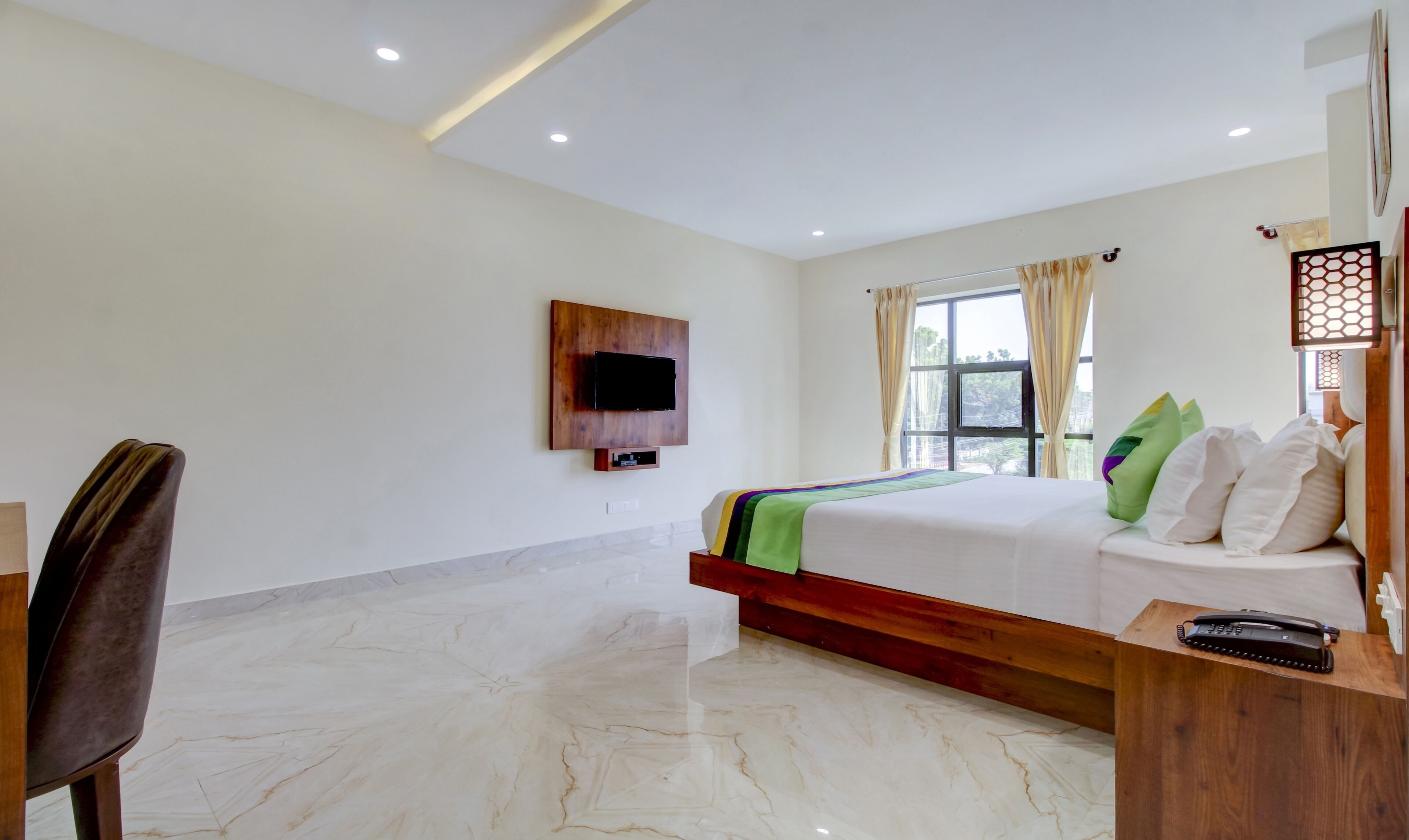 Une chambre d’hôtel équipée d’un lit, d’un bureau, d’une chaise, d’un téléviseur fixé au mur et d’une fenêtre avec des rideaux.