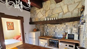 A kitchen with a stone wall, wooden ceiling beams, a white refrigerator, a microwave, and a coffee maker.