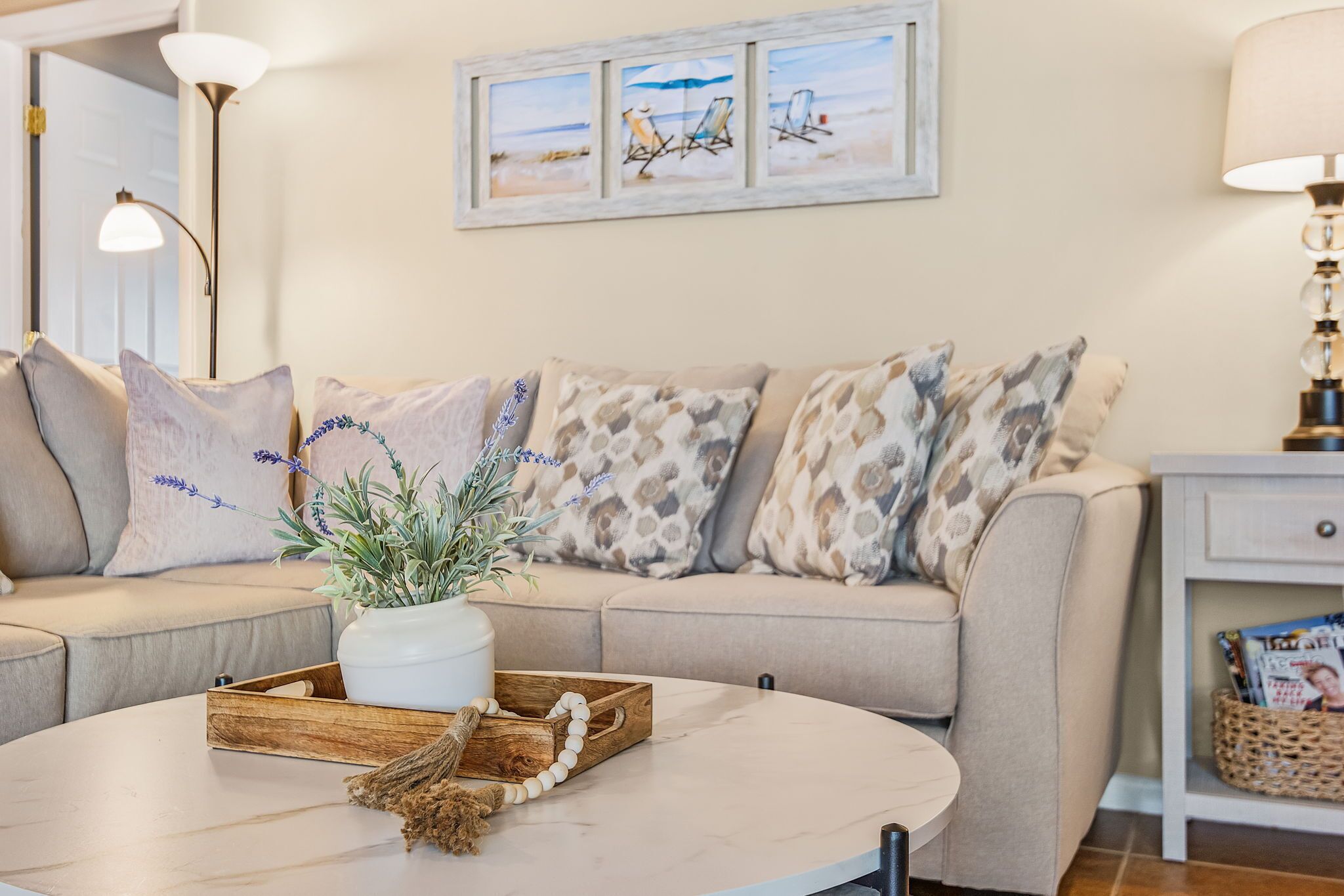Ein Wohnzimmer mit einem beigen Sofa, einem runden Couchtisch und einem Wandbild mit Strandstühlen.