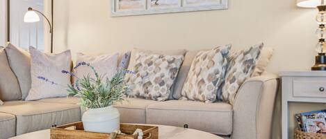 Ein Wohnzimmer mit einem beigen Sofa, einem runden Couchtisch und einem Wandbild mit Strandstühlen.